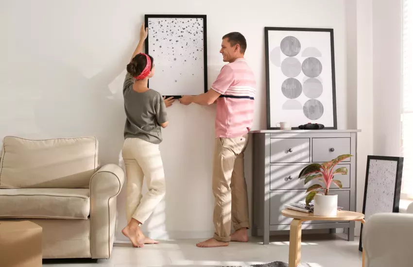 De voordelen van kunst in huis. Een man en vrouw die een kunstwerk in een kamer ophangen.